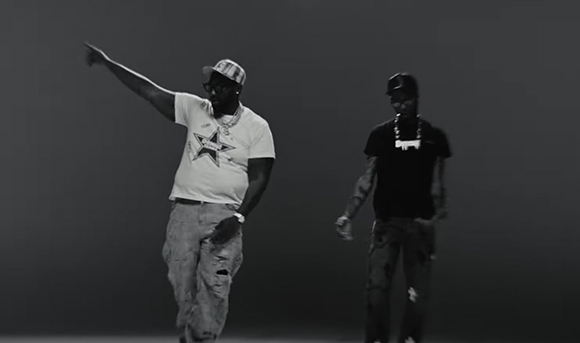Two men in streetwear posing against a dark background in black and white.