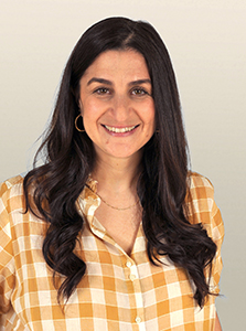 A smiling woman with long dark hair and gold hoop earrings wearing a yellow and white checkered shirt.