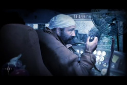 A man in a white head covering sits in a dimly lit vehicle cockpit, looking forward.