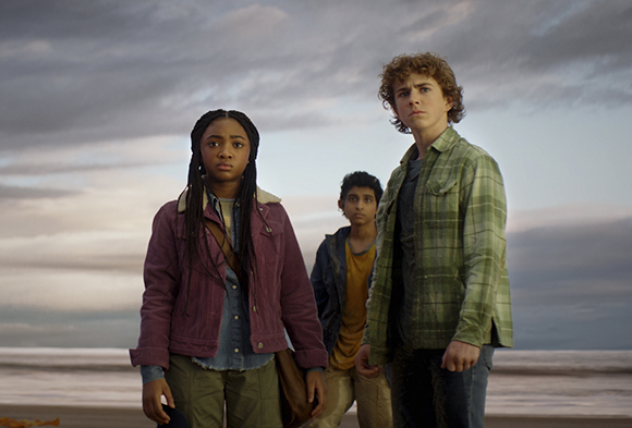 Three teenagers stand on a beach looking into the distance under a heavy, overcast sky.