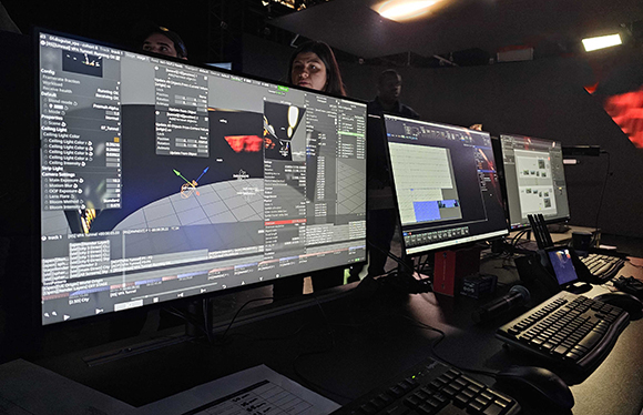 People working in a dark room with several large computer monitors displaying complex data and software.