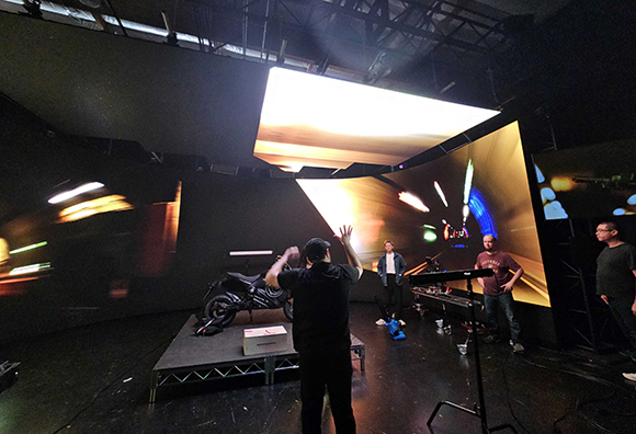Film crew in a dark studio surrounded by large, curved LED screens displaying bright, motion-blurred lights.