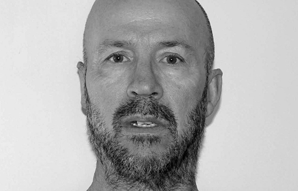 Black and white close-up portrait of a bald man with a beard looking directly at the camera.