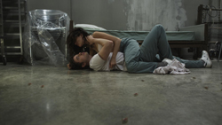 A person in a white shirt lies on the floor while another person in blue pants embraces them.