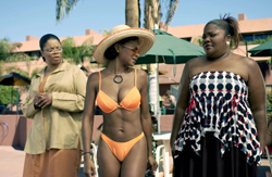 Three women standing together outdoors near green patio umbrellas and palm trees.