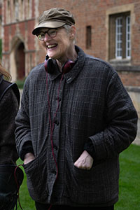 Smiling woman in a brown cap, glasses, and dark plaid jacket with headphones around her neck.