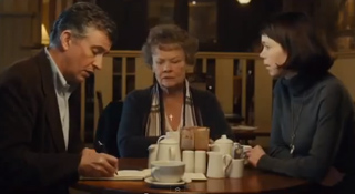 A man, an older woman, and a young woman sit at a table with coffee cups and sugar containers.