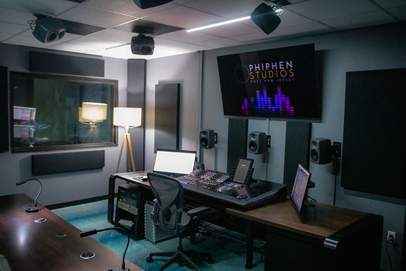 A recording studio control room featuring a mixing console, computer monitors, and acoustic wall panels.