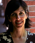 A smiling woman with dark, shoulder-length hair standing in front of a brick wall.