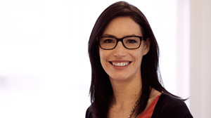 A smiling woman with dark hair and black-rimmed glasses looking at the camera.