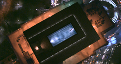 Aerial night view of a large building featuring a glowing dollar bill graphic on its rooftop.