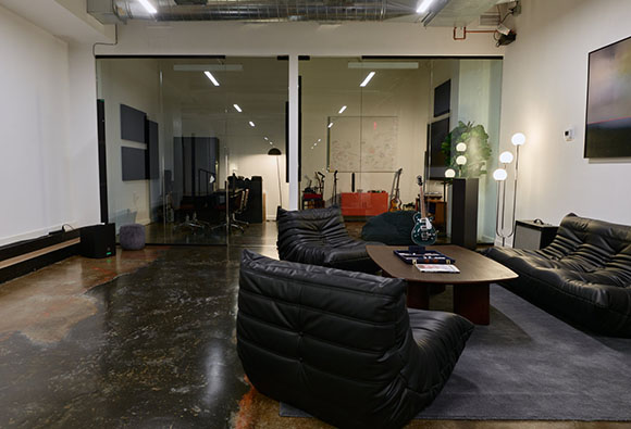 Black leather lounge chairs and a coffee table in a modern room with glass partitions and polished concrete floors.