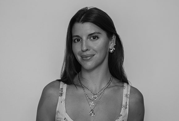 Black and white portrait of a woman with long dark hair, wearing layered necklaces and hoop earrings.