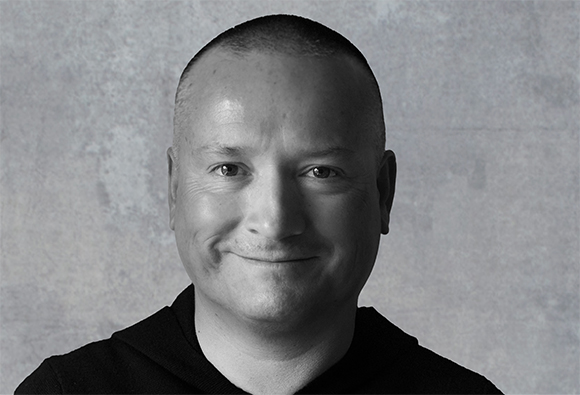 A black and white close-up portrait of a man smiling against a textured background.