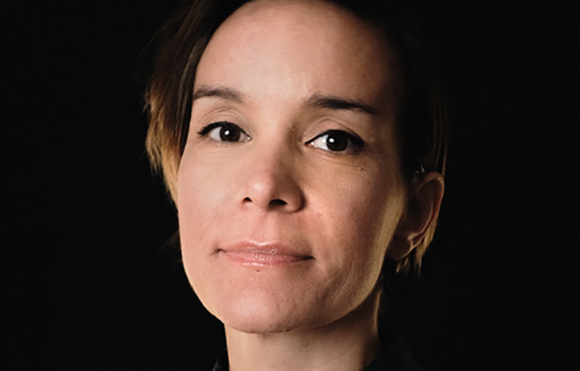 Close-up portrait of a person with short brown hair looking forward against a black background.