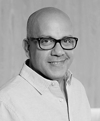 Black and white portrait of a bald man wearing glasses and a button-down shirt, smiling.
