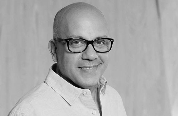 A bald man with glasses and a button-down shirt smiling slightly in a black and white portrait.