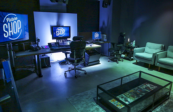 A dimly lit production studio featuring several computer monitors, desks, and office chairs.