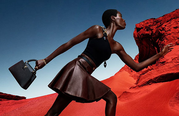 A woman in a black tank top and brown leather skirt poses against a bright red desert landscape.