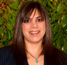 A smiling woman with straight dark hair and bangs wearing a dark shirt and a turquoise pendant necklace.
