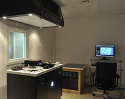 A dark editing room with a large film processing machine, a computer workstation, and an office chair.