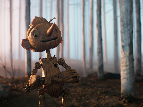 A wooden puppet with a long nose and large eyes stands in a foggy forest of tall, thin trees.