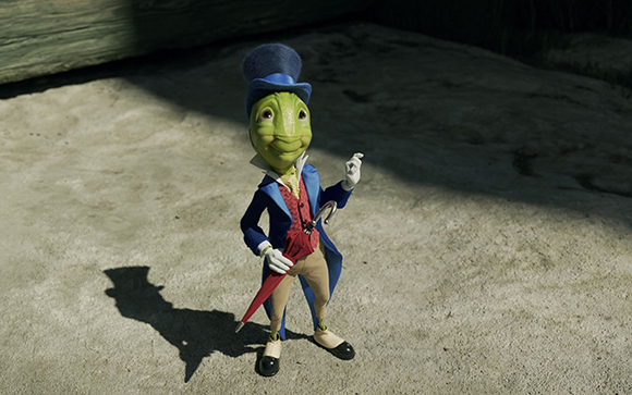 An anthropomorphic green frog wearing a blue top hat, blue tailcoat, and red vest, holding a red umbrella.