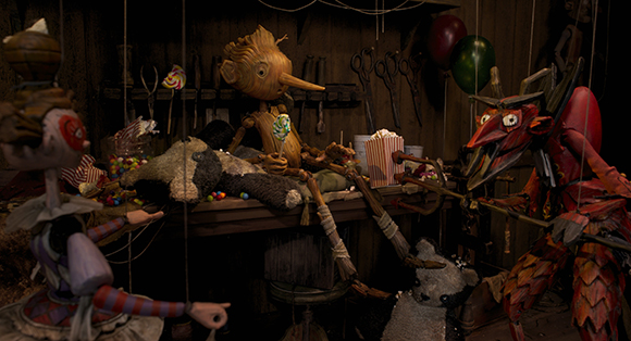 Various wooden and fabric puppets sit around a table filled with candy and popcorn in a dark room.