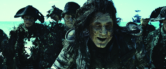 A group of dark, seaweed-covered figures with weathered skin staring intensely toward the camera.