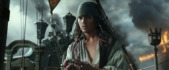 A man with dreadlocks and a bandana looks intensely forward on a ship amidst smoke and clouds.