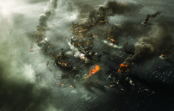 Aerial view of several large sailing ships engaged in a battle on a dark sea with heavy smoke and fires.