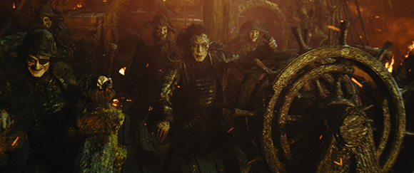 Skeletal figures in dark clothing stand on a wooden ship deck amidst fire and embers.