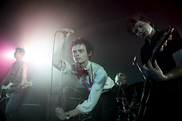 A four-piece rock band performs on a dark stage under bright spotlights.
