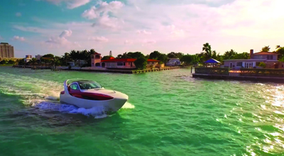 A white and red motorboat creates a wake as it travels through turquoise water near a coastal town.