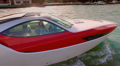 A red and white motorboat with two people on board moves through turquoise water.