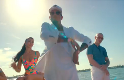 A man in a white shirt and sunglasses stands outdoors with a woman in a colorful swimsuit and a man in a blue polo.