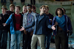 A group of young men standing in a semi-circle, singing with expressive facial expressions.