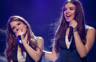 Two women with long hair singing into handheld microphones under blue stage lighting.