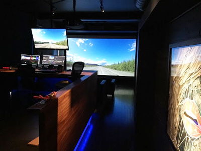 A dark editing studio with a large projection screen showing a road and several computer monitors.