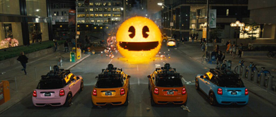 Four colorful Mini Coopers parked facing a massive, glowing yellow smiley face on a city street at night.
