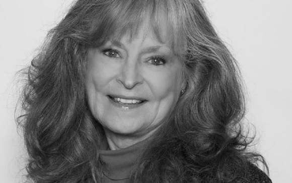A smiling woman with long, wavy hair looks toward the camera in a black and white portrait.