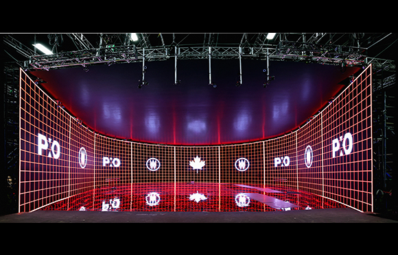 A curved, red-lit grid display featuring various white logos in a dark, large-scale indoor space.
