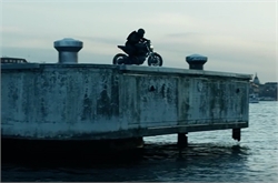 A person riding a motorcycle on a weathered concrete pier overlooking the water at dusk.