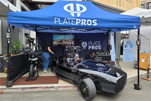 A black car parked under a blue canopy with the text PLATEPROS printed on it.