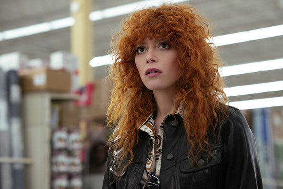 A woman with voluminous, curly red hair wearing a black leather jacket in a store.