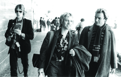 Black and white photo of three men walking outdoors on a city street.