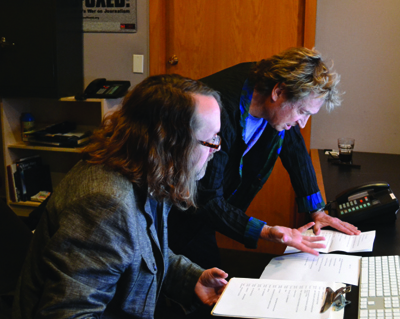 Two men lean over a desk to look at papers and a computer keyboard.