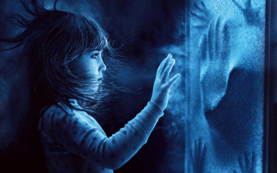 A young girl reaches her hand toward a glass pane covered in handprints in a dark, blue-toned setting.