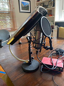 A studio microphone with a pop filter and a large LED light panel mounted on a stand on a wooden table.