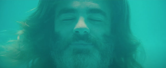 Close-up of a man with long hair and a beard underwater with eyes closed.